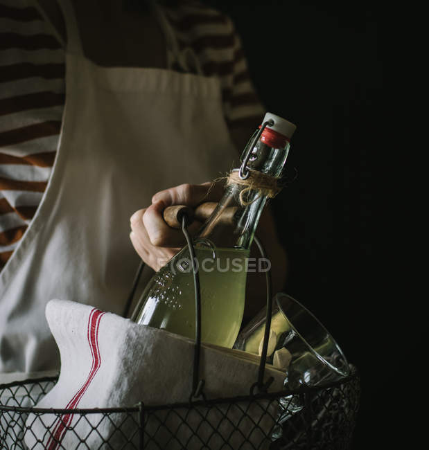 Крупный план женской руки, несущей корзину с бутылкой сиропа бузины, полотенцем и стеклом — стоковое фото