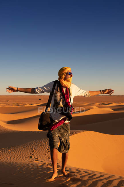 Unrecognizable tourist with outstretched arms standing against bright cloudless sundown sky in desert — Stock Photo