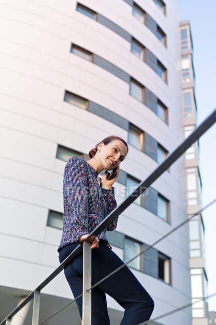 Empreendedora mulher alegre sorrindo e olhando para longe enquanto conversa no smartphone — Fotografia de Stock