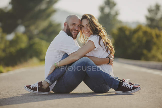 Affectionate couple embracing close sitting on rural road — Stock Photo