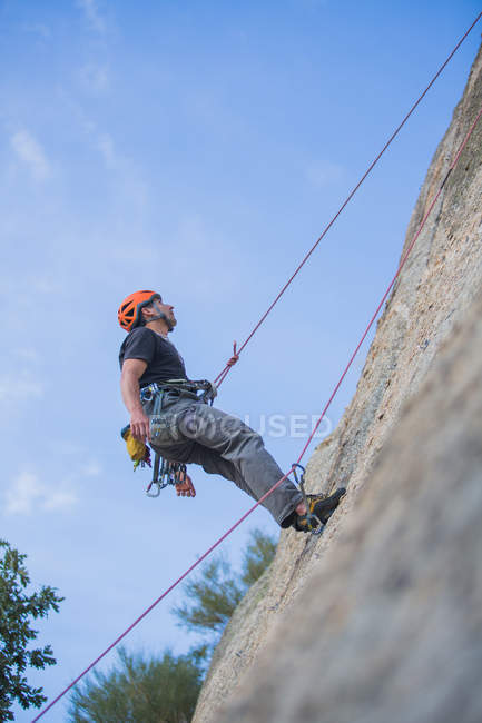 Da sotto l'uomo scalare una roccia in natura con attrezzatura da arrampicata — Foto stock