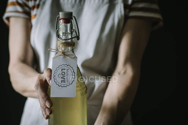 Midsection of woman holding bottle of elderflower wine with Made with love label — Stock Photo
