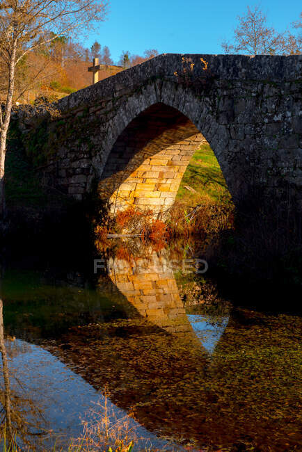 Ponte de pedra envelhecida sobre o rio tranquilo no dia ensolarado na pitoresca paisagem de outono — Fotografia de Stock