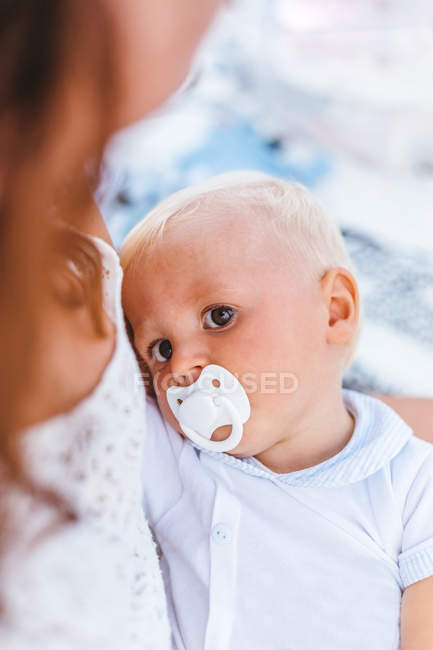 Retrato de un bebé rubio con un chupete tomado con su madre antes de irse a dormir - foto de stock