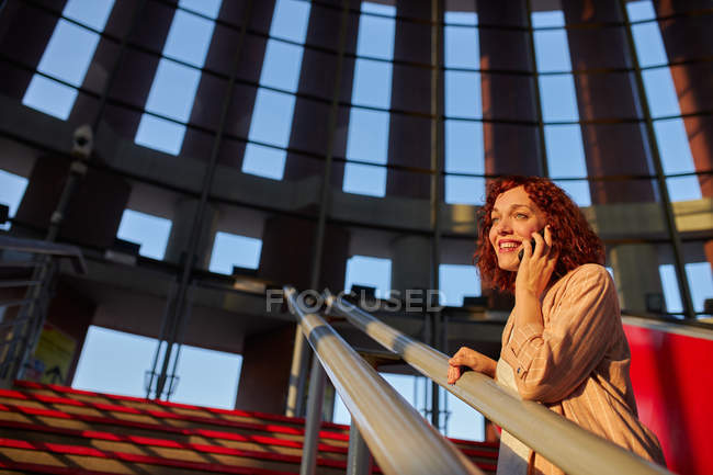 Charming red haired young woman talking on phone in airport while waiting for train to departure — Stock Photo