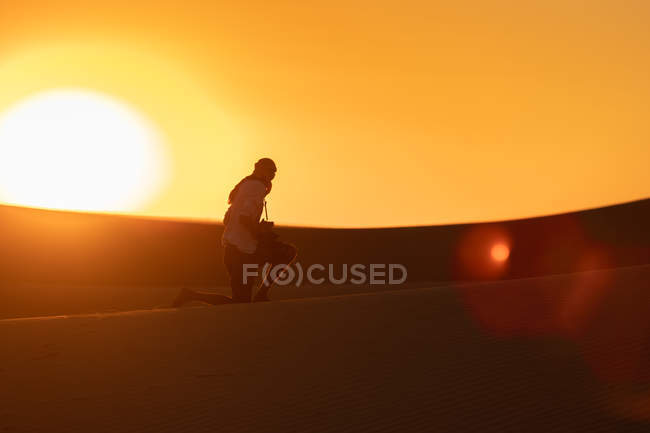 Una silueta de viajero irreconocible que toma fotos de dunas mientras se apoya en la arena en un desierto asombroso. - foto de stock