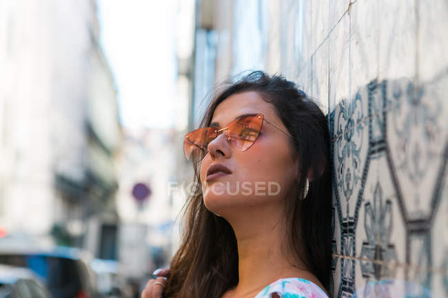 Mulher linda pacífica na roupa da moda e óculos de sol brilhantes em pé ao lado de azulejos parede exótica na rua cênica — Fotografia de Stock