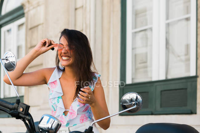 Красива смішна жінка в сонцезахисних окулярах дивиться на дзеркало мотоцикла на вулиці — стокове фото