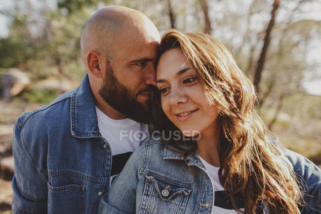 Happy loving couple in denim jackets cuddling while sitting close in countryside on sunny day — Stock Photo