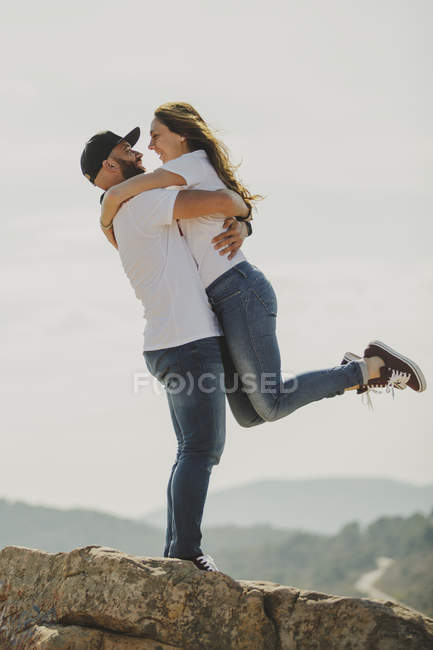 Side view of romantic cheerful couple in matching outfit hugging and looking at each other while standing at hilly slope — Stock Photo