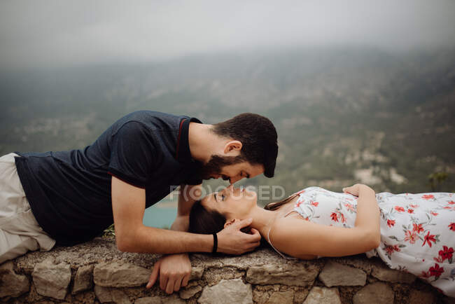Ласковая пара отдыхает, лежа на каменном заборе в горах — стоковое фото