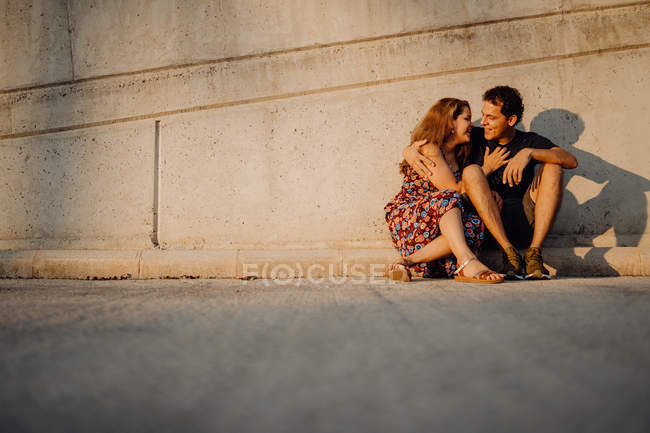 Man and woman looking at each other and embracing sitting at nearby street wall — Stock Photo