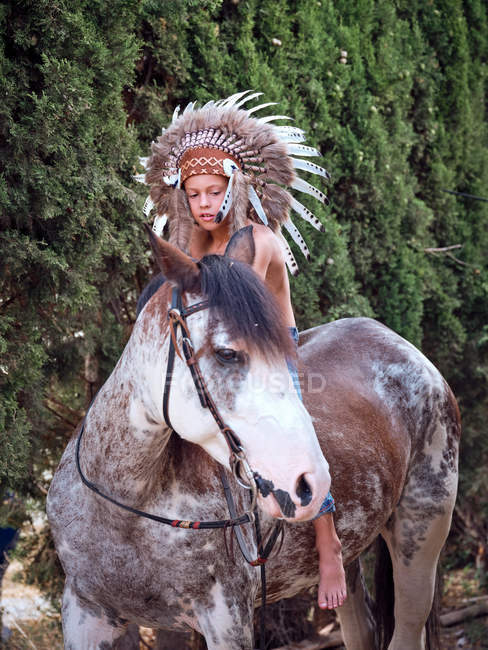 Sério menino no autêntico indiana pena chapéu equitação cavalo no parque — Fotografia de Stock