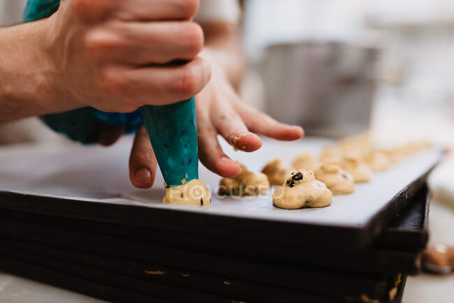Cuisinier anonyme pressant de la pâte fraîche sur un plateau avec du papier tout en travaillant sur un fond flou de boulangerie — Photo de stock