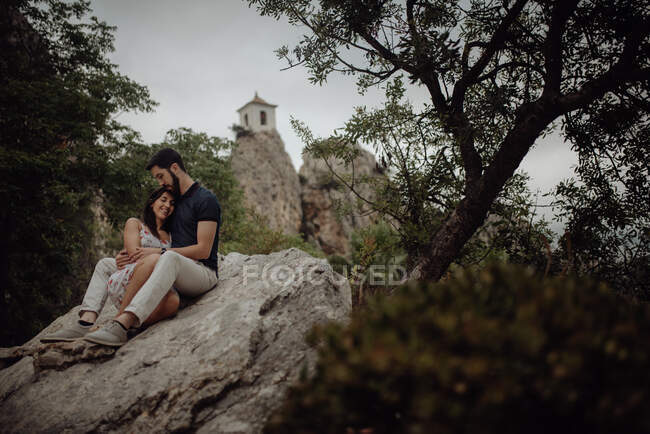 Romantic couple resting on rock surrounded with trees — Stock Photo