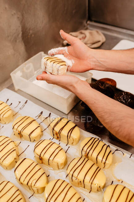 Anonymous male cook spreading coconut flakes on sides of tasty patisserie over table in bakery — Stock Photo
