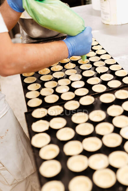Зверху анонімний працівник в рукавичці кладе свіжі лісові горіхи на смачну солодку випічку на лоток під час роботи в пекарні — стокове фото