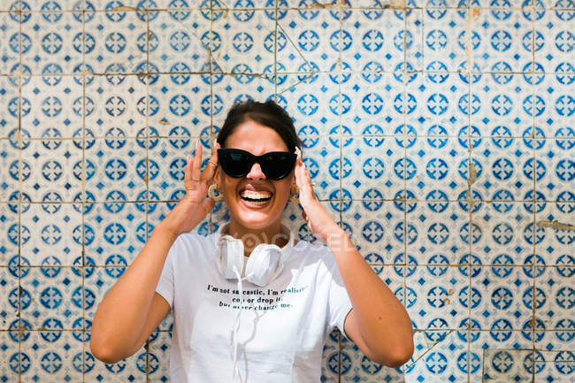 Красива жінка в повсякденному вбранні і навушники з стоячи на синій мозаїчній стіні будівлі на міській вулиці — стокове фото