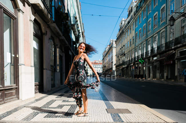 Verspielte Frau im langen Kleid dreht sich um, während sie die Sommerstraße der Stadt entlangläuft — Stockfoto