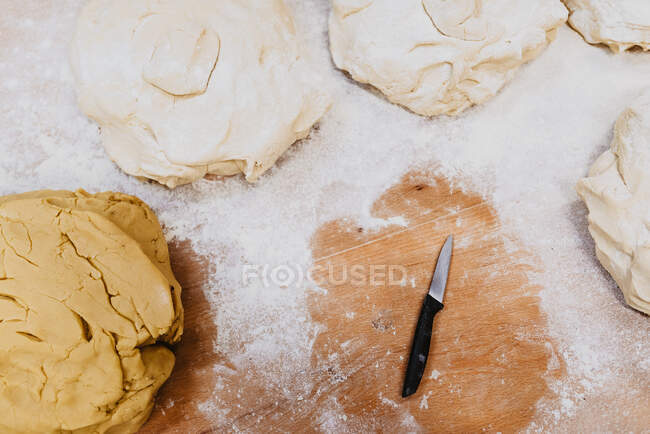 D'en haut petit couteau placé sur la table de bois près de la pâte fraîche et la farine de blé renversé dans la cuisine — Photo de stock