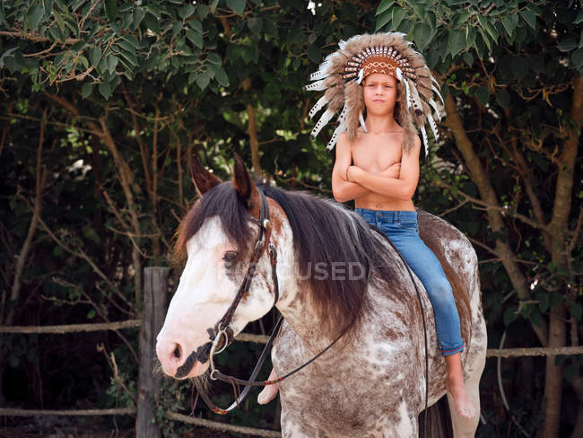 Ernster Junge mit echtem indischen Federhut reitet Pferd im Park — Stockfoto