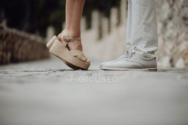 Crop side view of woman in sandals standing on tiptoe in front of casual man on pebbled pavement — Stock Photo