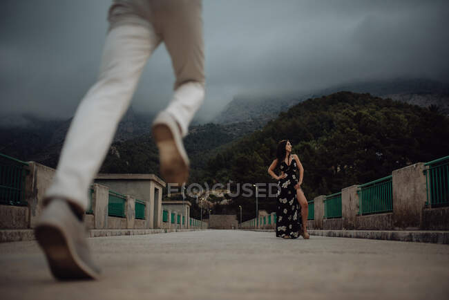 Чоловік біжить на побачення з красивою жінкою, що стоїть у довгій сукні на кам'яному мосту — стокове фото