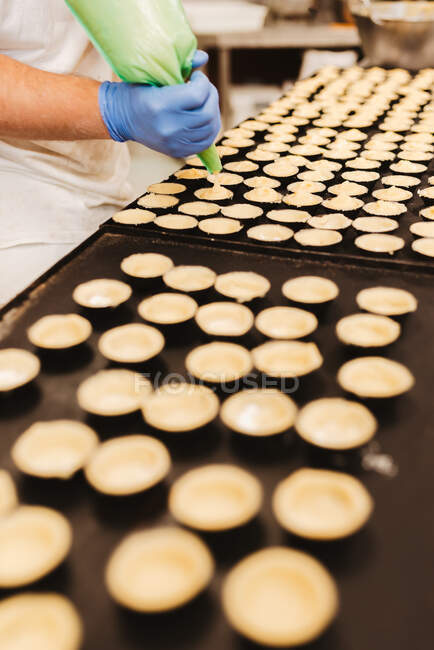 Cocinero anónimo exprimiendo masa de pastelería fresca en bandeja con papel - foto de stock