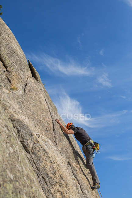 D'en bas l'homme escalade un rocher dans la nature avec des équipements d'escalade — Photo de stock
