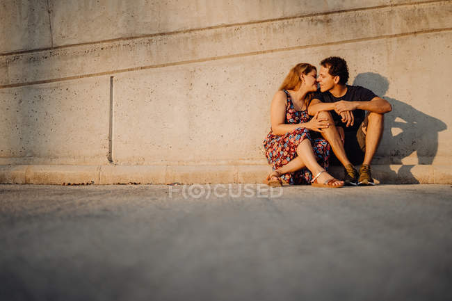 Uomo e donna guardarsi l'un l'altro e baciarsi seduti alla vicina parete stradale — Foto stock