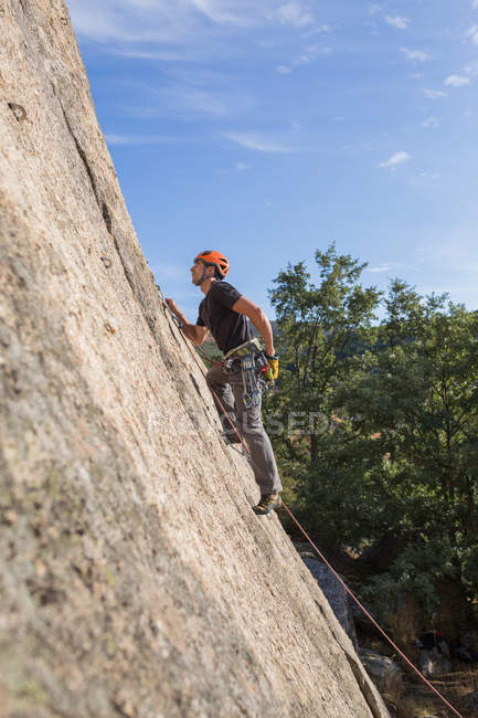 Da sotto l'uomo scalare una roccia in natura con attrezzatura da arrampicata — Foto stock