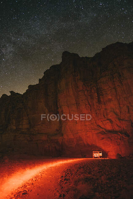 Vehicle parked near rough cliff during trip through Wadi Rum desert at starry night in Jordan — Stock Photo