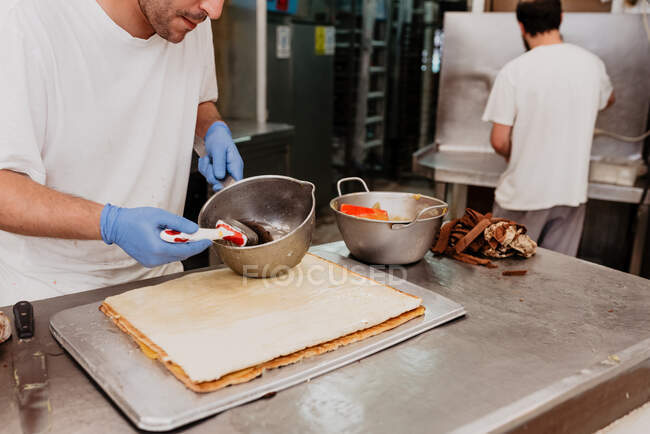Bäckereiangestellte in Latexhandschuhen verteilt süße Marmelade auf frischem Brötchen über die Küchentheke — Stockfoto