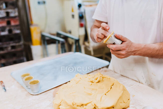 Crop man in white t-shirt putting fresh dough into cups while making pastry in kitchen of bakery — Stock Photo