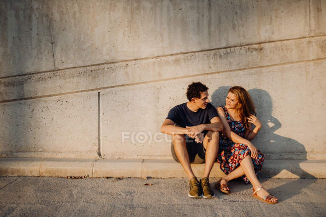 Hombre y mujer mirándose los unos a los otros sentados cerca de la pared de la calle - foto de stock