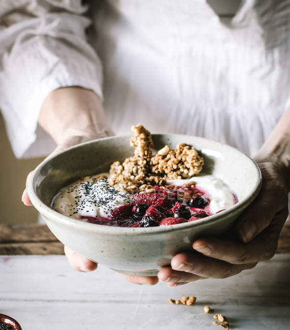 Hands of woman holding bowl with delicious crispy granola served with fresh berries, yogurt and chia seeds — Stock Photo