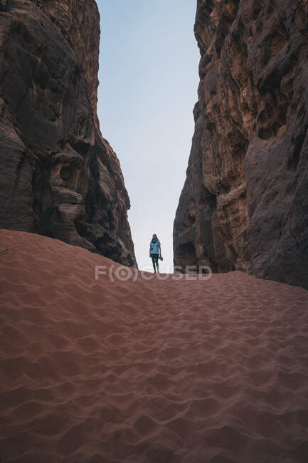 Anonimo turista donna in piedi sulla sabbia tra muri di pietra grezza contro cielo blu senza nuvole nel burrone del deserto Wadi Rum in Giordania — Foto stock