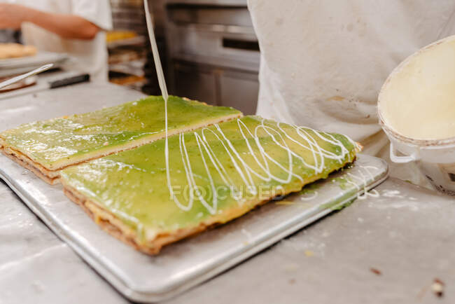 Unbekannter Konditor im Handschuh dekoriert leckeren frischen Kuchen mit Gebäckkrümeln während er in der Küche der Bäckerei arbeitet — Stockfoto