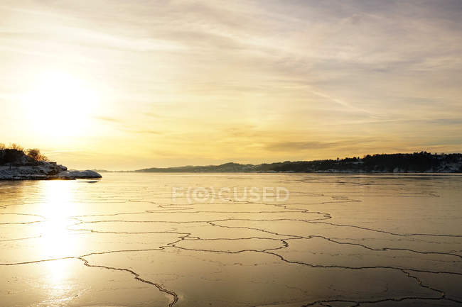 Rio largo de tirar o fôlego com derretimento e rachaduras camada de gelo lisa sob majestoso céu colorido por do sol — Fotografia de Stock