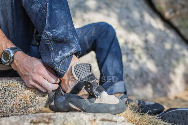 Обрезанный образ скалолаза надевая обувь альпинистов, чтобы начать восхождение — стоковое фото