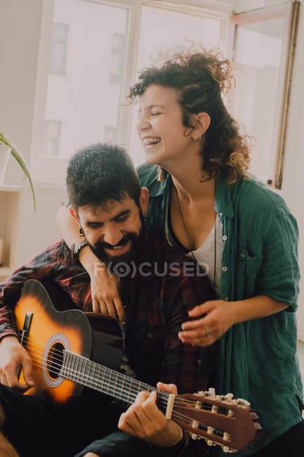 Нежная веселая пара в повседневных нарядах, играющая дома на гитаре — стоковое фото