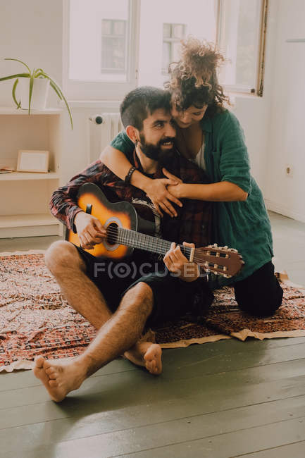 Tender alegre casal em roupas casuais tocando guitarra em casa — Fotografia de Stock