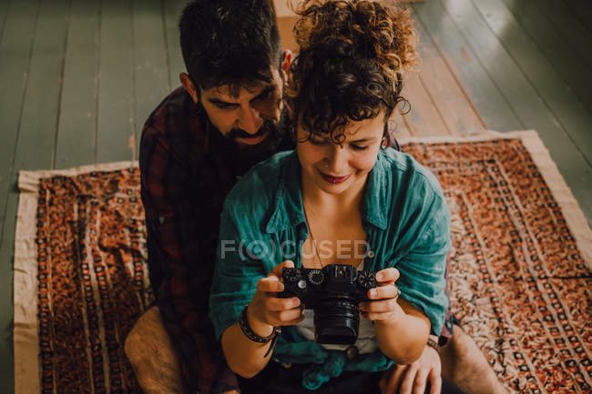 Dall'alto vista di hipster uomo e donna coppia utilizzando la fotocamera seduta a piedi nudi sul pavimento dell'appartamento — Foto stock