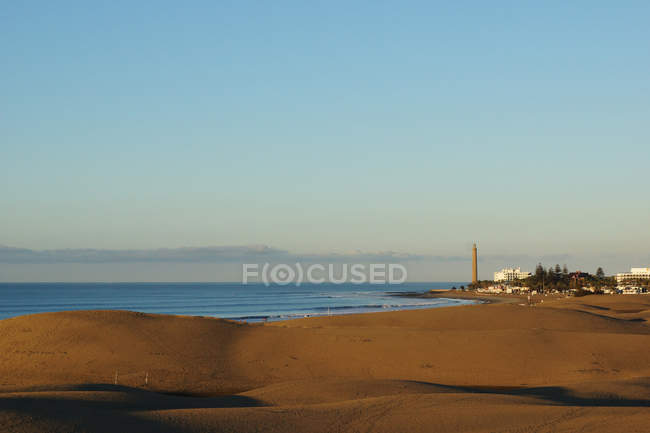 Пустое мирное побережье с синим морем и отдаленным городом в солнечный день — стоковое фото