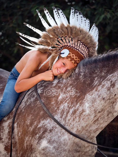 Joyeux garçon en authentique chapeau de plume indien équitation cheval dans le parc — Photo de stock