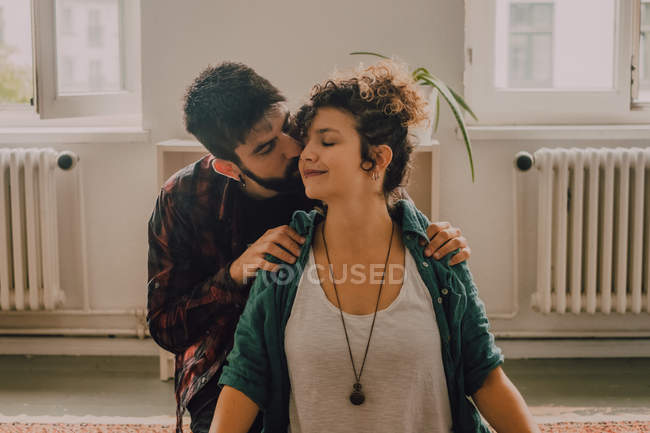 Man in casual clothing massaging shoulders of relaxed woman sitting in lotus position on floor at home — Stock Photo