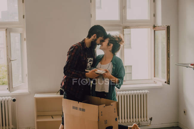 Hipster couple unpacking together boxes while standing barefoot in light room and cuddling — Stock Photo