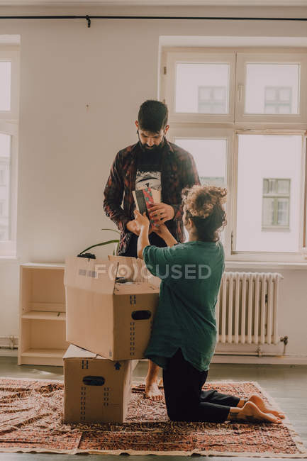 Hipster couple unpacking together boxes while standing barefoot in light room — Stock Photo