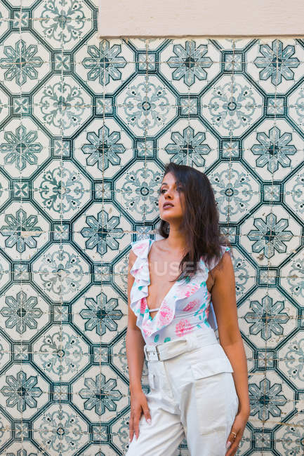 Peaceful gorgeous woman in trendy outfit standing beside tiled exotic wall on scenic street — Stock Photo