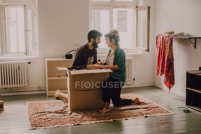 Весела пара сміється, сидячи поруч з відкритими картонними коробками в сучасній квартирі — стокове фото